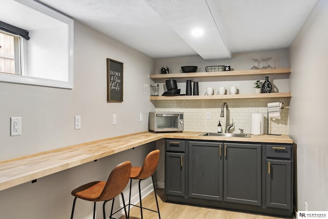 bar featuring tasteful backsplash, wooden counters, light wood-type flooring, gray cabinetry, and sink