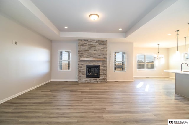 unfurnished living room with a stone fireplace, sink, wood-type flooring, a chandelier, and a raised ceiling