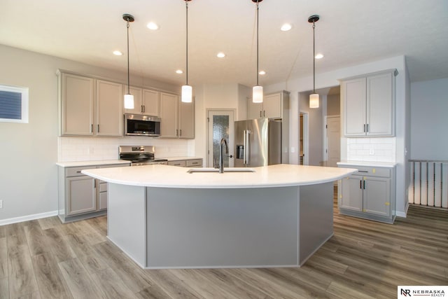 kitchen featuring stainless steel appliances, an island with sink, hanging light fixtures, and gray cabinetry