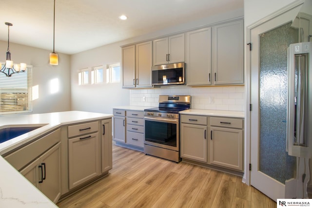 kitchen featuring pendant lighting, gray cabinetry, backsplash, stainless steel appliances, and light wood-type flooring