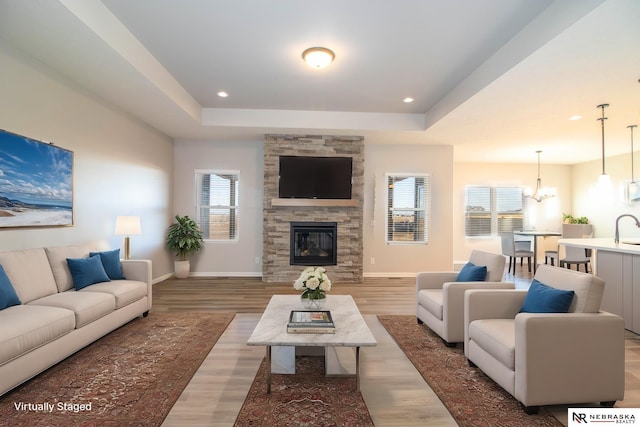 living room with sink, hardwood / wood-style flooring, an inviting chandelier, a fireplace, and a raised ceiling