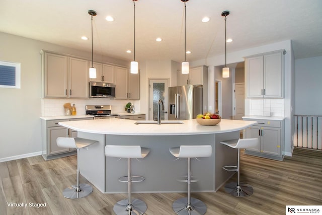 kitchen with pendant lighting, stainless steel appliances, sink, and a kitchen island with sink