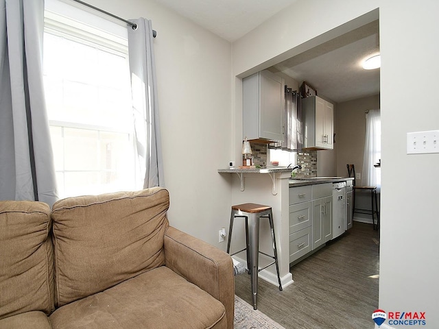 kitchen with dishwasher, dark wood-type flooring, tasteful backsplash, kitchen peninsula, and a breakfast bar area