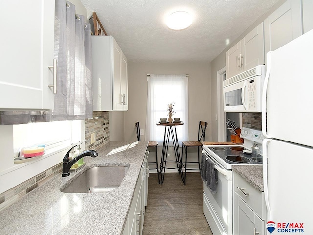 kitchen featuring decorative backsplash, light stone counters, white appliances, sink, and white cabinetry