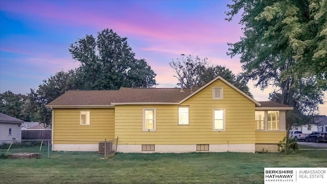 back house at dusk featuring a lawn and central air condition unit