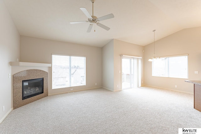 unfurnished living room with vaulted ceiling, a wealth of natural light, light carpet, and ceiling fan with notable chandelier