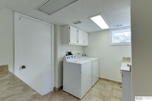 clothes washing area featuring a textured ceiling, separate washer and dryer, and cabinets