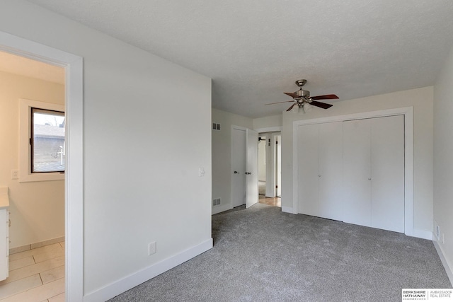 unfurnished bedroom featuring ceiling fan, a closet, light carpet, and a textured ceiling