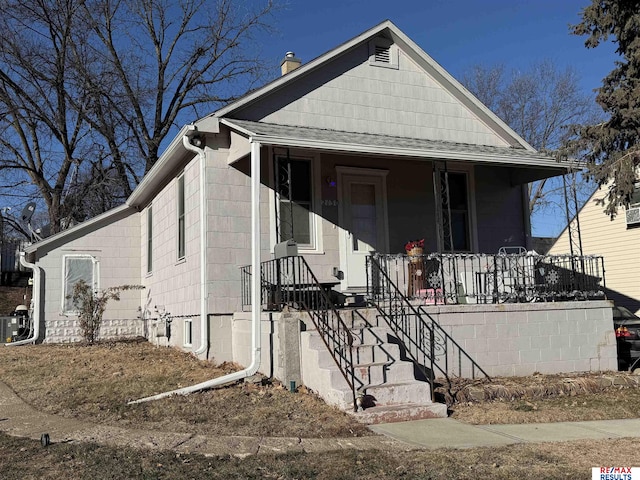 view of front of house featuring cooling unit, roof with shingles, a porch, and a chimney