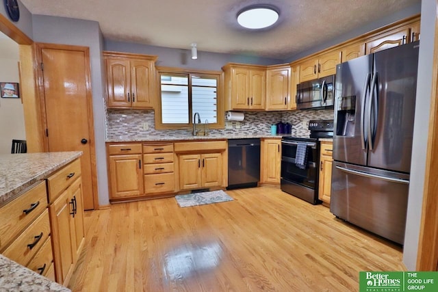 kitchen with black appliances, backsplash, light wood-type flooring, and sink