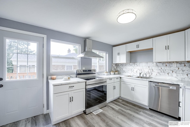 kitchen with white cabinetry, sink, wall chimney exhaust hood, a healthy amount of sunlight, and appliances with stainless steel finishes