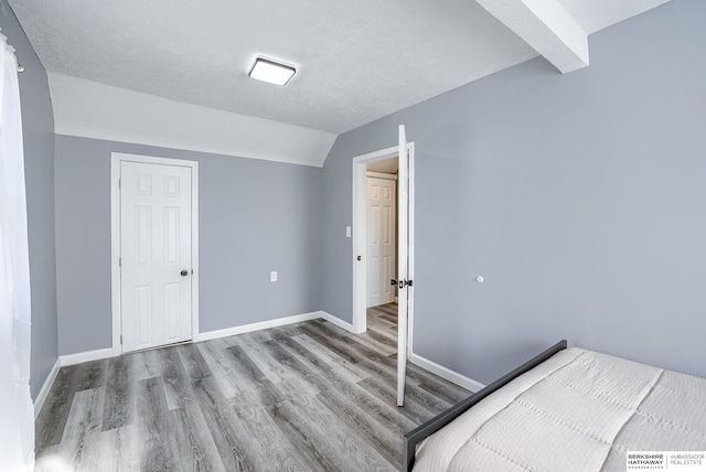 unfurnished bedroom featuring hardwood / wood-style floors, vaulted ceiling with beams, and a textured ceiling