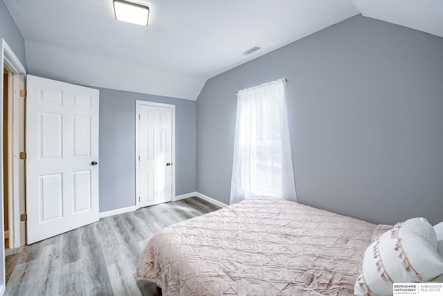 bedroom with a closet, light hardwood / wood-style flooring, and vaulted ceiling