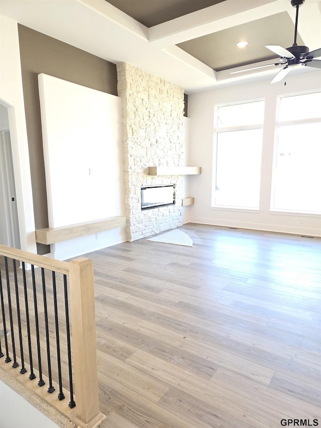 unfurnished living room featuring a stone fireplace, ceiling fan, and wood finished floors