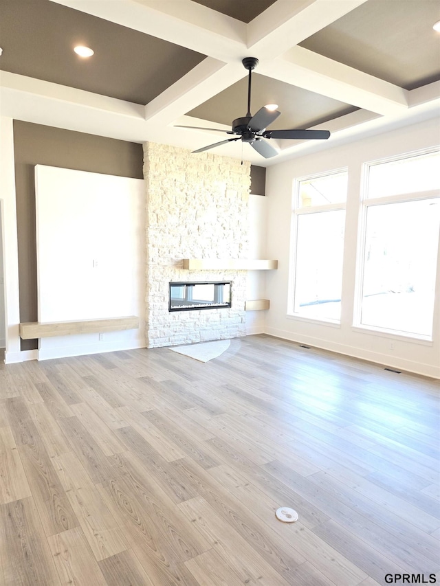 unfurnished living room with a stone fireplace, coffered ceiling, ceiling fan, and wood finished floors