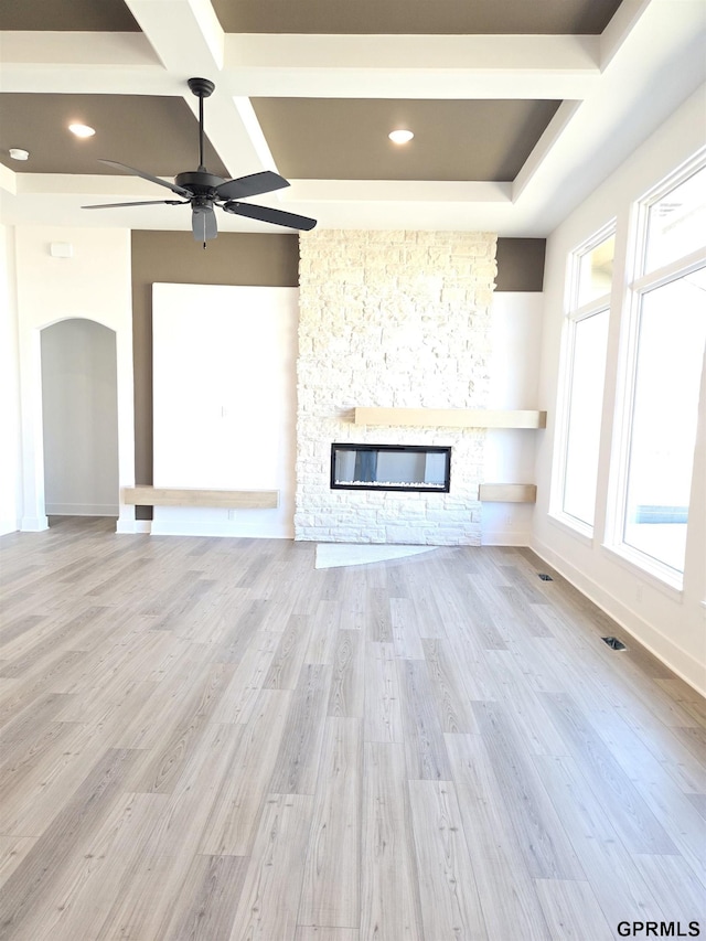 unfurnished living room featuring baseboards, ceiling fan, a stone fireplace, wood finished floors, and arched walkways