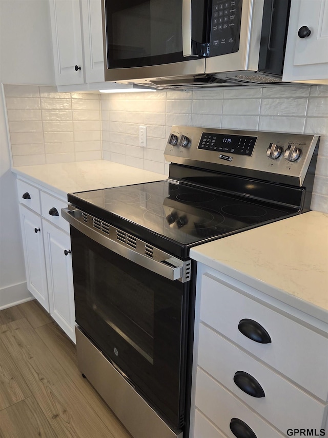 kitchen with backsplash, white cabinetry, stainless steel appliances, and wood finished floors