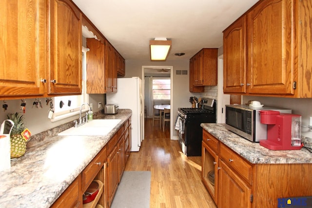 kitchen with appliances with stainless steel finishes, light wood-type flooring, light stone counters, and sink