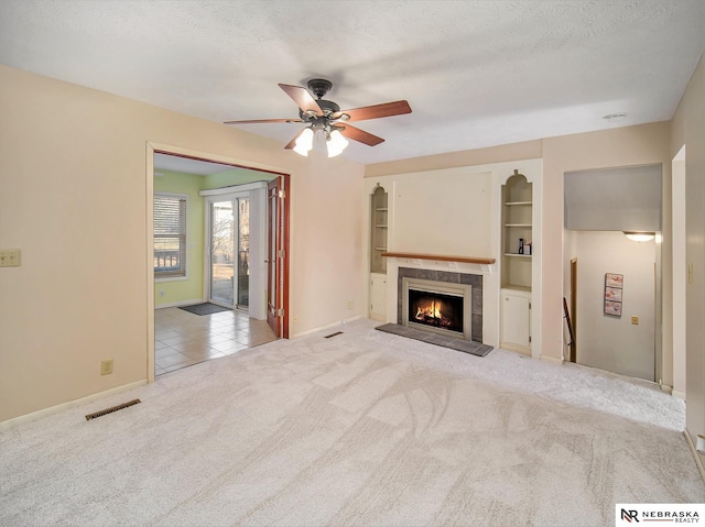 unfurnished living room with light carpet, a tiled fireplace, built in features, and a textured ceiling