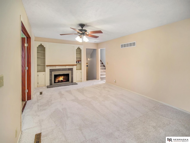 unfurnished living room with ceiling fan, a tiled fireplace, light carpet, and a textured ceiling