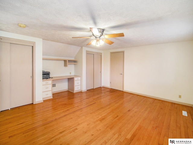 unfurnished living room with ceiling fan, built in desk, a textured ceiling, and light wood-type flooring