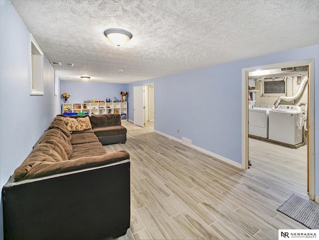 living room with a textured ceiling, washing machine and clothes dryer, and light hardwood / wood-style floors