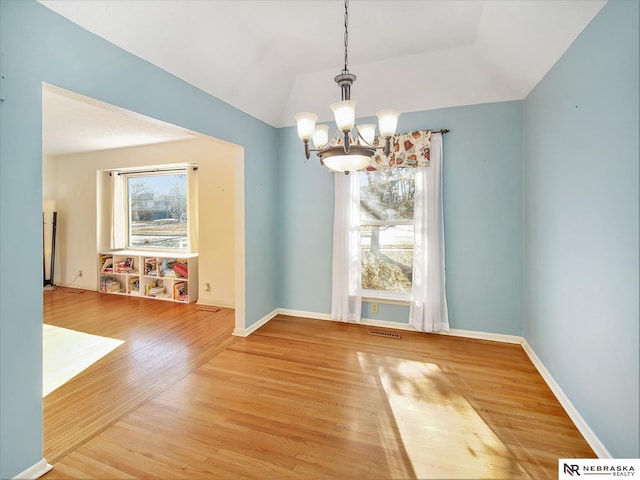 unfurnished dining area featuring hardwood / wood-style flooring, lofted ceiling, and an inviting chandelier