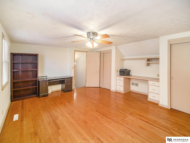 unfurnished office with ceiling fan, built in desk, a textured ceiling, and light hardwood / wood-style flooring