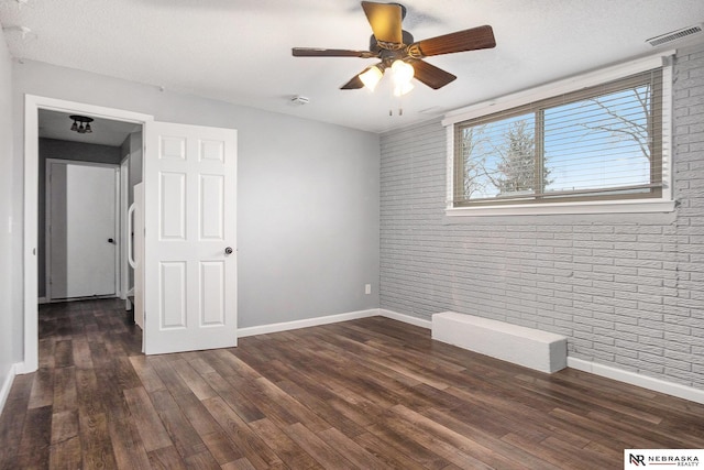 empty room featuring a textured ceiling, ceiling fan, brick wall, and dark hardwood / wood-style floors