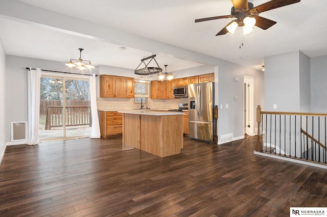 kitchen with dark wood-type flooring, decorative backsplash, decorative light fixtures, a kitchen island, and stainless steel appliances