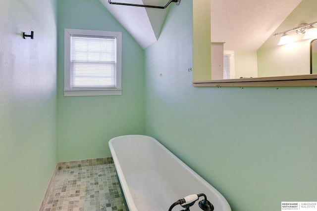 bathroom featuring a bath, vaulted ceiling, and a textured ceiling