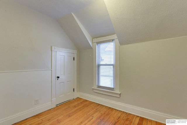 additional living space featuring light wood-type flooring, vaulted ceiling, and a textured ceiling