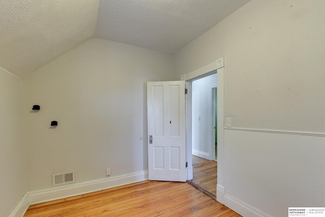 spare room featuring light hardwood / wood-style floors, a textured ceiling, and vaulted ceiling