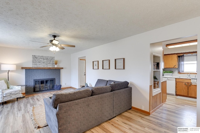 living room featuring a textured ceiling, ceiling fan, sink, a fireplace, and light hardwood / wood-style floors