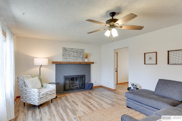 living room with a fireplace, a textured ceiling, light hardwood / wood-style flooring, and ceiling fan