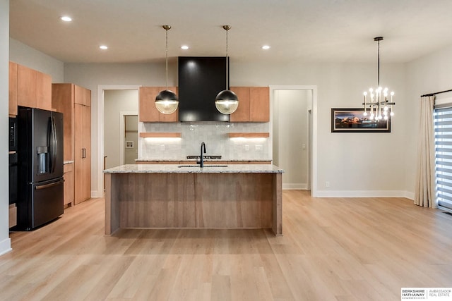 kitchen with light wood-type flooring, decorative light fixtures, black refrigerator with ice dispenser, and light stone counters