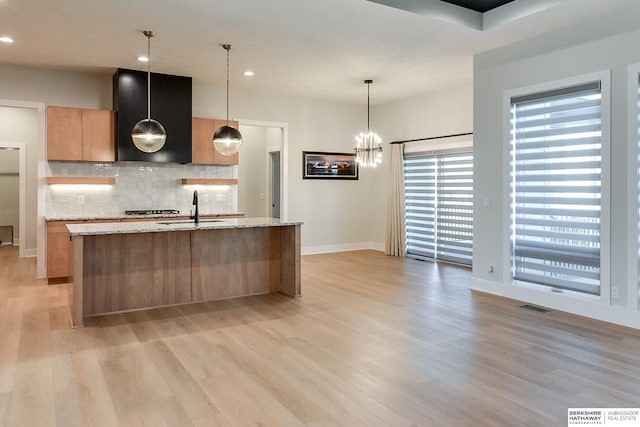 kitchen with light stone counters, sink, decorative light fixtures, and ventilation hood