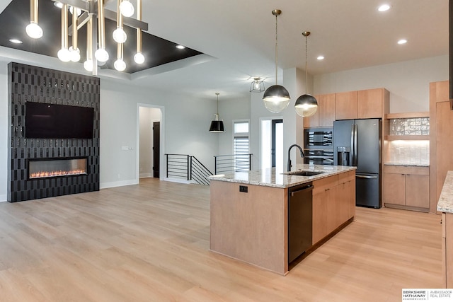 kitchen featuring dishwasher, a center island with sink, sink, stainless steel fridge, and decorative light fixtures