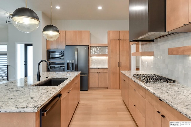 kitchen featuring appliances with stainless steel finishes, sink, wall chimney range hood, pendant lighting, and a center island with sink