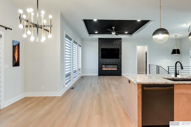 kitchen featuring stainless steel dishwasher, a tray ceiling, sink, decorative light fixtures, and a fireplace