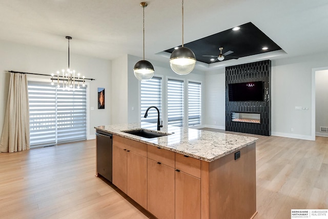 kitchen with a center island with sink, ceiling fan with notable chandelier, sink, a tray ceiling, and light stone counters