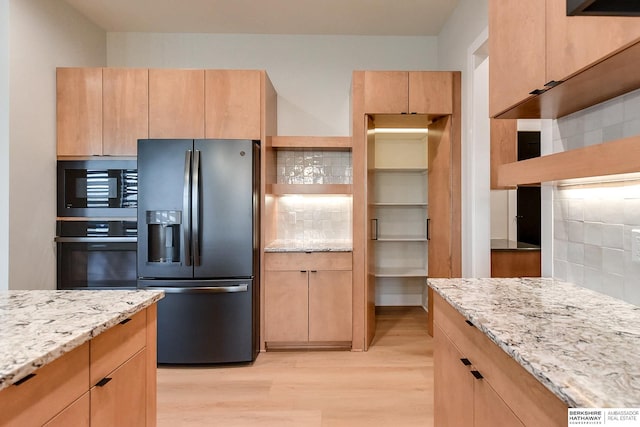 kitchen featuring decorative backsplash, stainless steel fridge, light stone countertops, wall oven, and black microwave