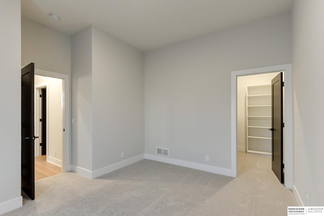 unfurnished bedroom with a walk in closet, a closet, and light colored carpet