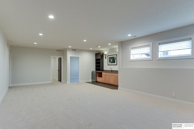 unfurnished living room featuring indoor wet bar, light colored carpet, and beverage cooler