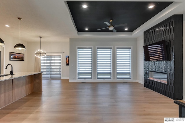 unfurnished living room featuring ceiling fan with notable chandelier, a large fireplace, a raised ceiling, and sink