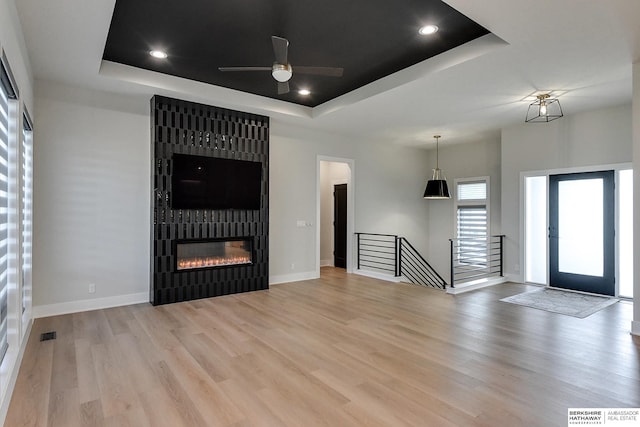 unfurnished living room featuring a raised ceiling, ceiling fan, a fireplace, and light hardwood / wood-style floors