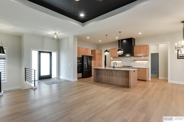 kitchen featuring hanging light fixtures, light stone counters, light hardwood / wood-style flooring, a kitchen island with sink, and black appliances