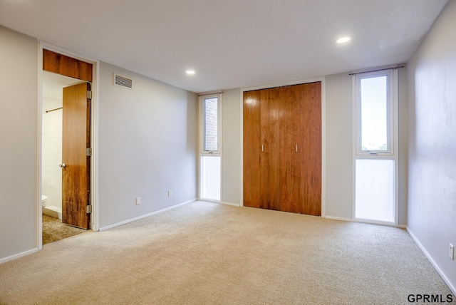 unfurnished bedroom with a closet, light colored carpet, connected bathroom, and multiple windows