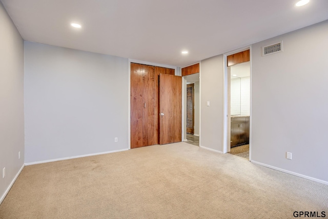 unfurnished bedroom featuring a closet, light carpet, and ensuite bath