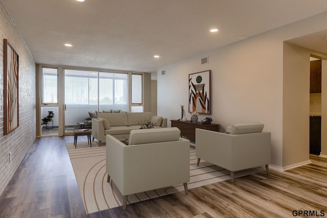 living room with light hardwood / wood-style flooring, a wall of windows, and brick wall